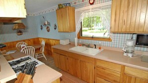 A kitchen with wooden cabinets, a sink, a stove, and a window with a view of trees. - Seidls (Cable)
