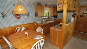 A kitchen with wooden cabinets, a dining table with chairs, and a hanging light fixture. - Seidls (Cable)