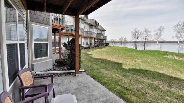 A covered porch with outdoor seating, a view of a lake, and a multi-story building with a balcony. - Unit 311 1 BD/ 1 BA Condo (Birchwood)