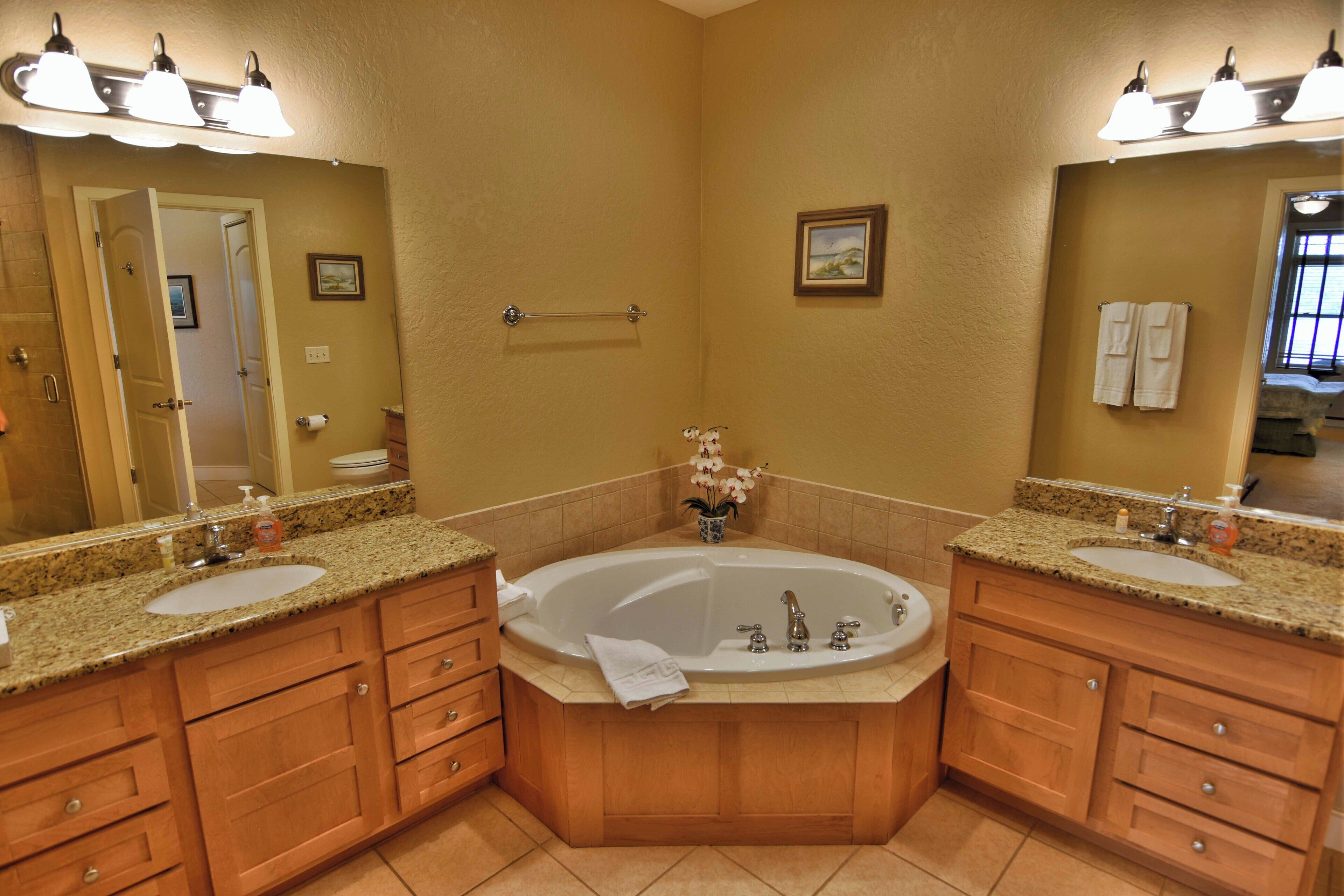 A bathroom with two sinks, a large bathtub, wooden cabinets, and a mirror.