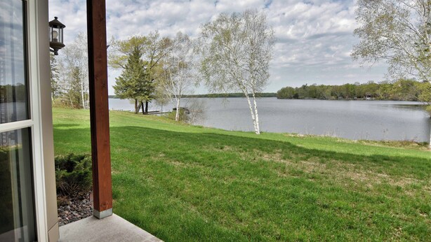 Une vue sur le lac depuis une véranda dotée d’une balustrade en bois, d’une lampe et d’une pelouse verdoyante.