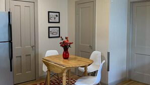 A compact kitchen with a dining table, chairs, a ceiling fan, and a refrigerator.