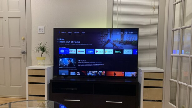 A flat-screen TV on a black entertainment unit in a room with a patterned rug and a potted plant.