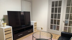 A living room with a flat-screen TV, a glass coffee table, a black sofa, and a patterned rug.