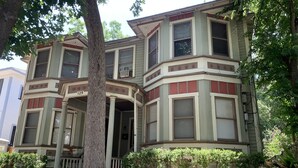 A Victorian-style house with bay windows, a prominent front porch, and a large tree in front.