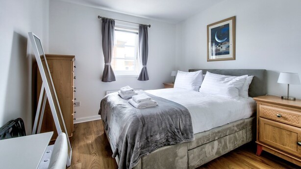 Et pænt hotelværelse med seng, sengebord og et vindue med gardiner.