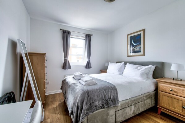 A neatly arranged hotel room with a bed, bedside table, and a window with curtains. - GuestReady - 2BR in Leith w Ocean Views & Parking (Leith)
