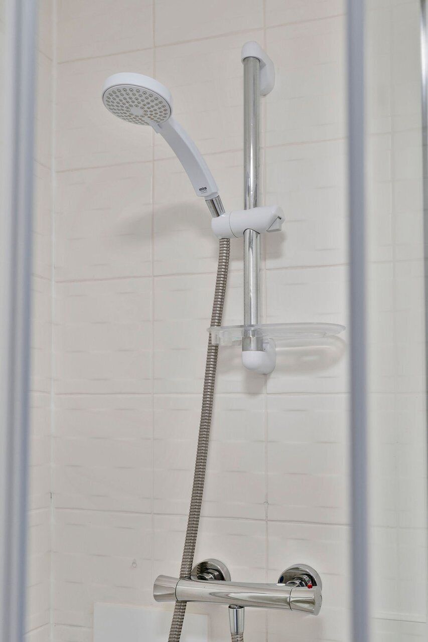 A shower with a handheld showerhead and a wall-mounted faucet.