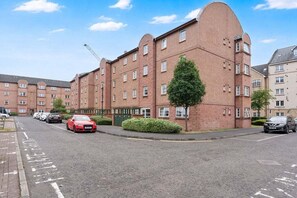 A multi-story brick building with a curved corner, a tree in front, and cars parked on the street. - GuestReady - 2BR in Leith w Ocean Views & Parking (Leith)