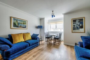 A living room with a blue sofa, a dining table with chairs, and two framed pictures on the walls.