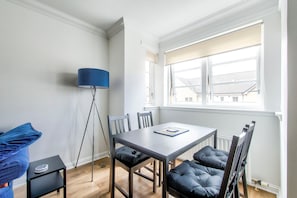 A modern dining area with a table and chairs, a floor lamp, and a view of the outside through a window.