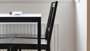 Et værelse med et vindue der kigger ud over et boligområde, en radiator og et bord med stole.