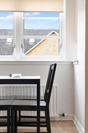 Ein Zimmer mit Fenster und Blick auf eine Wohngegend, inklusive Heizkörper und einem Tisch mit Stühlen.