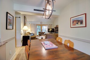 Un comedor con una mesa de madera, sillas, una lámpara y obras enmarcadas en las paredes.