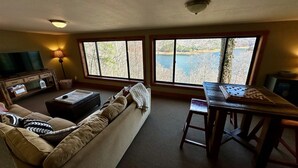 A living room with a sofa, a coffee table, a TV, and a large window overlooking a lake.