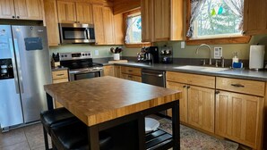 A modern kitchen with wooden cabinets, stainless steel appliances, a wooden table, and a window with curtains.