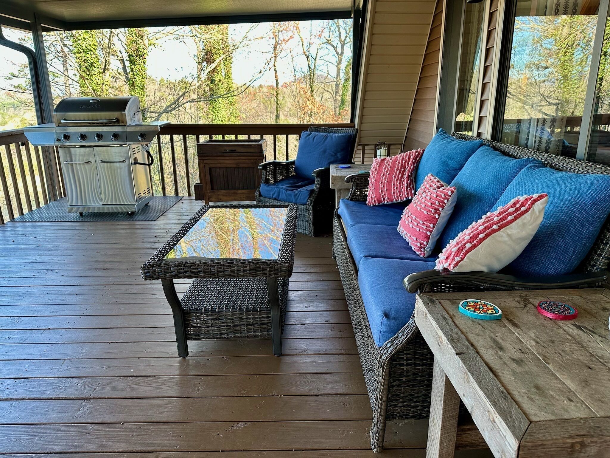 Una terrazza coperta con barbecue, mobili in vimini e vista sugli alberi.