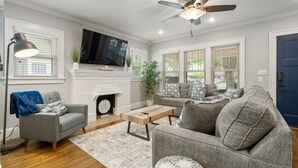 Ein Wohnzimmer mit Kamin, grauen Sofas, einem Couchtisch und einem Deckenventilator.