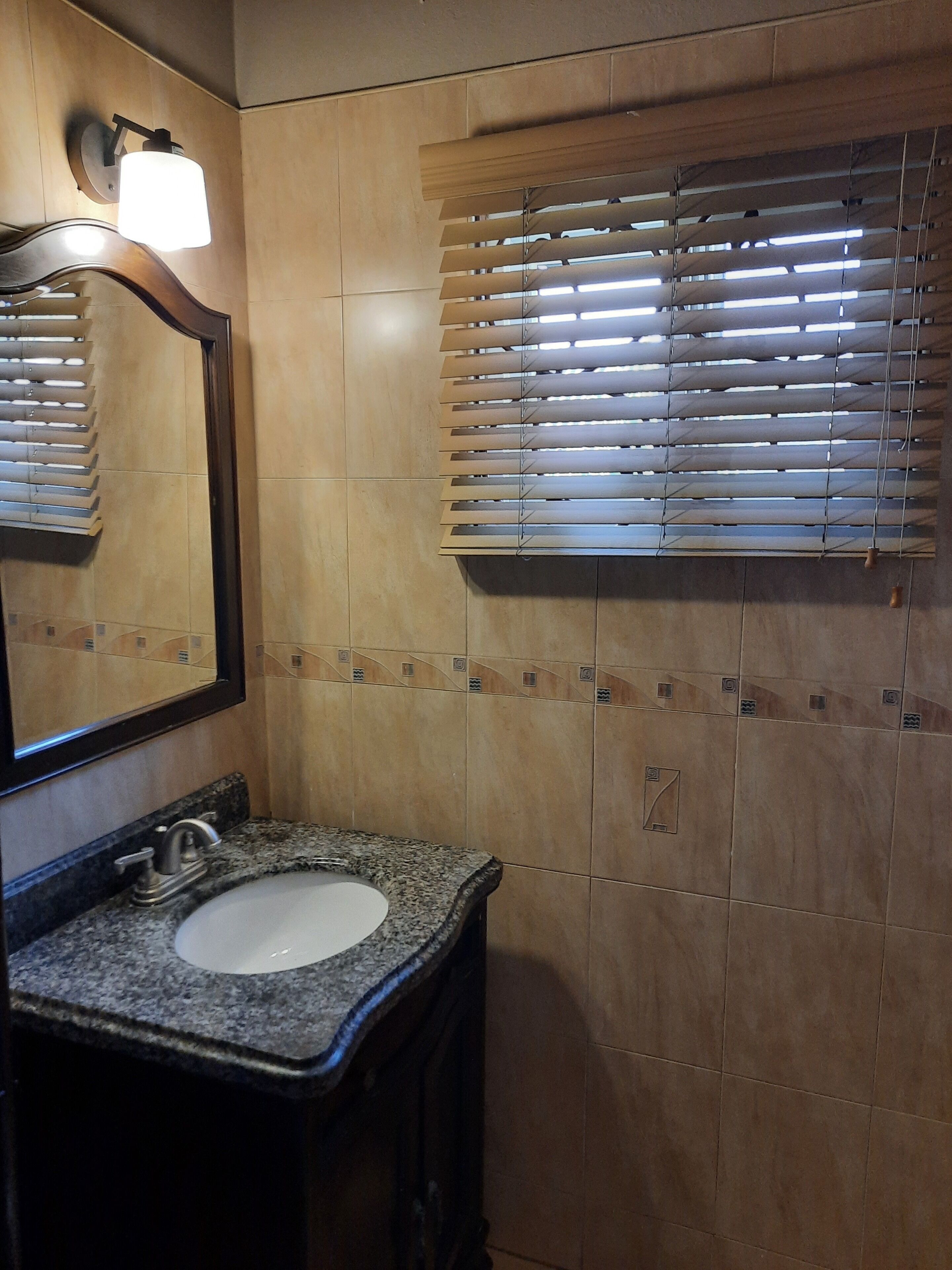 A bathroom with a granite sink, a mirror, and wooden blinds.