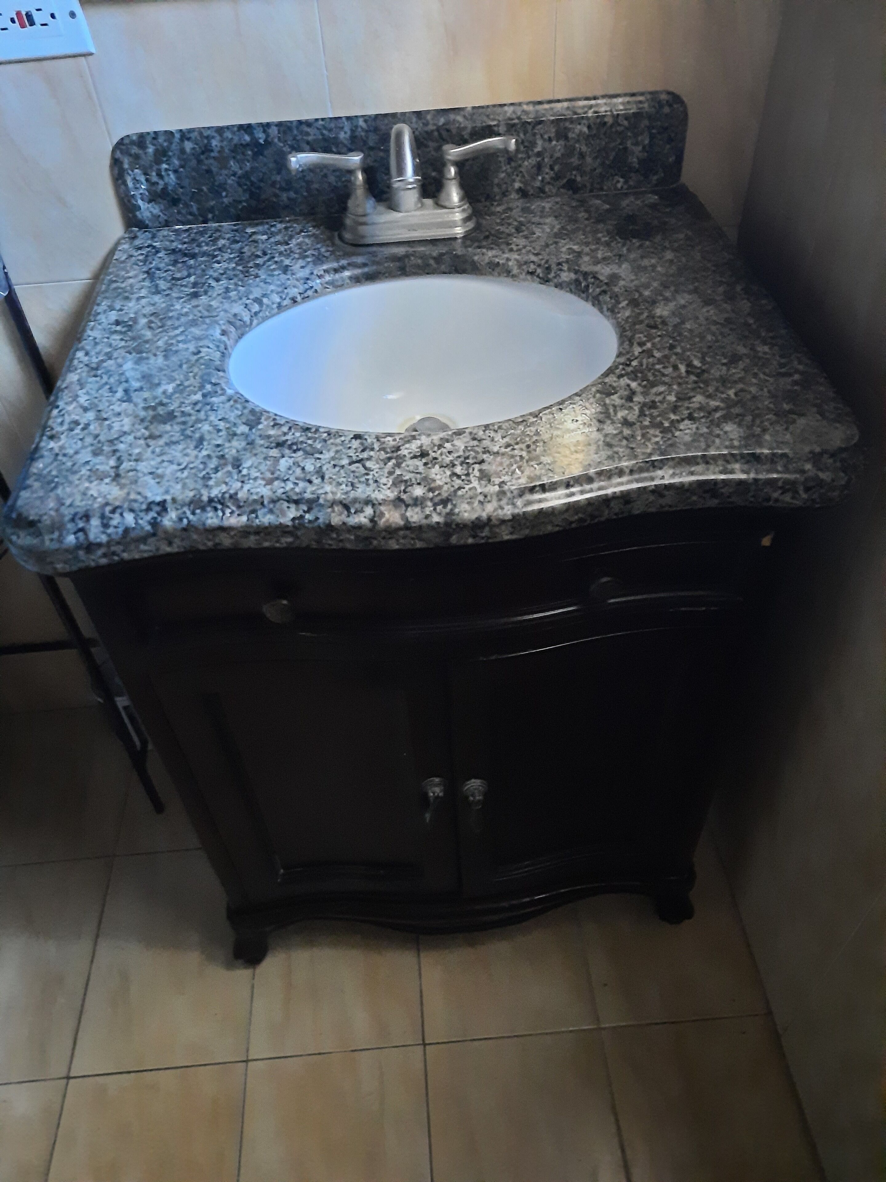A bathroom with a granite countertop, a white sink, and dark cabinetry.