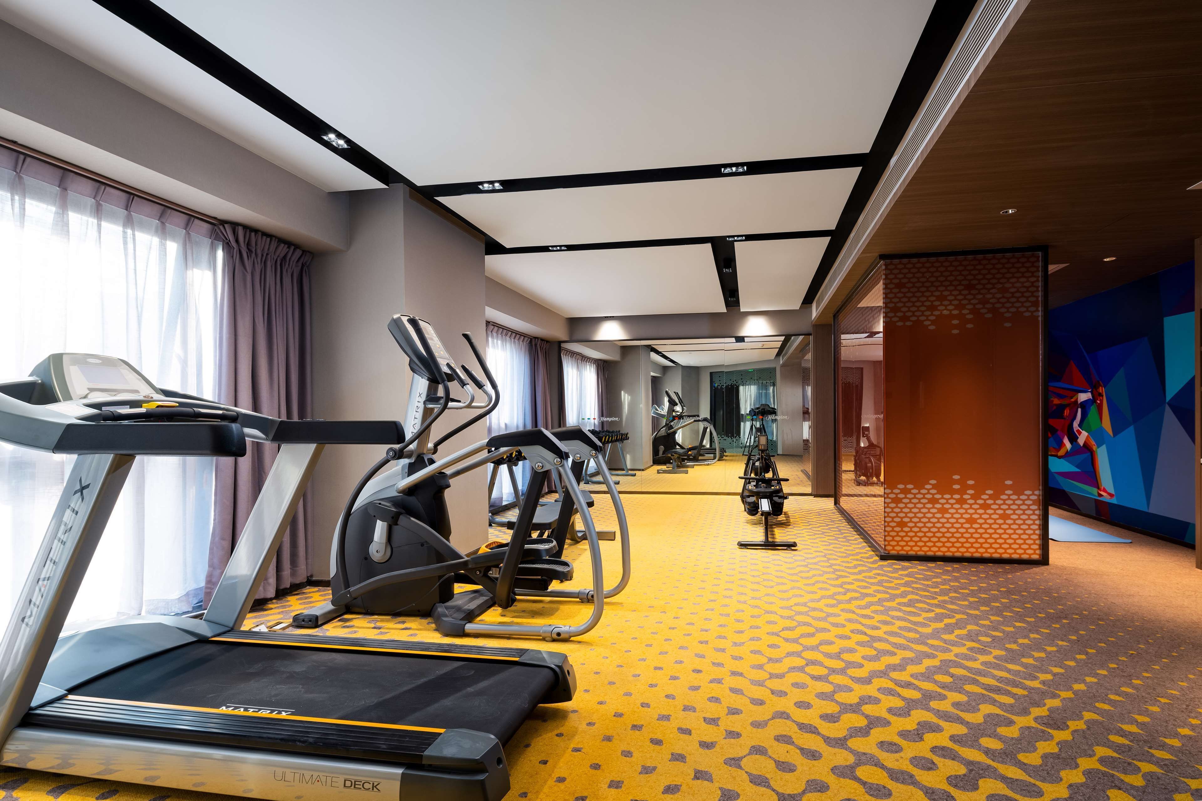 Un gimnasio de hotel con cintas de correr, elípticas y un espejo grande.