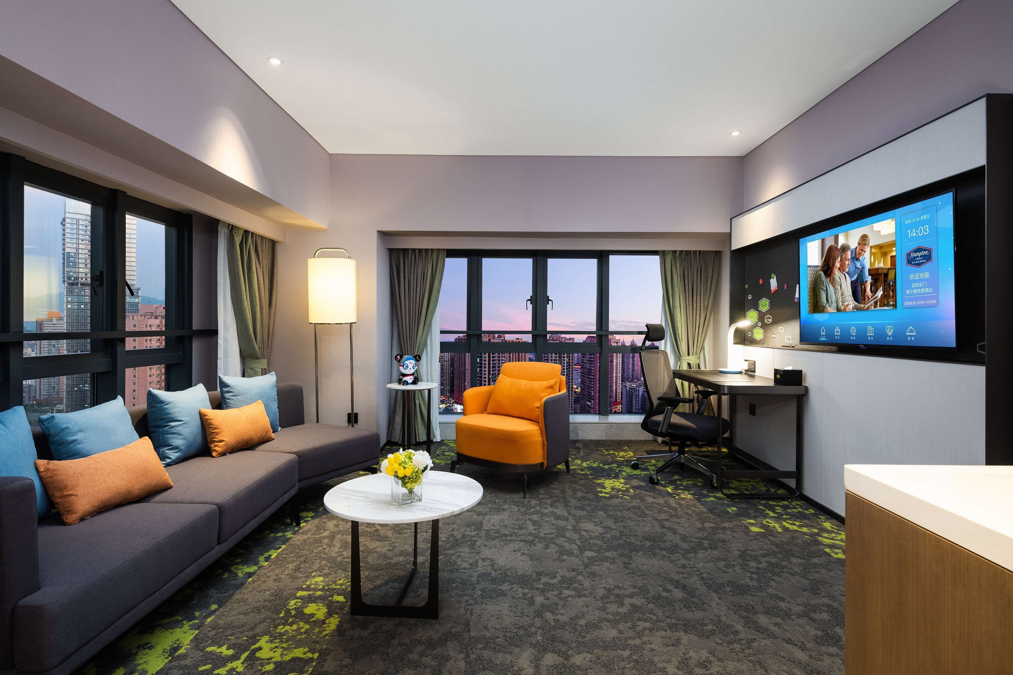 Une chambre d’hôtel moderne équipée d’une grande télévision, d’un canapé, d’un fauteuil orange et d’un bureau.