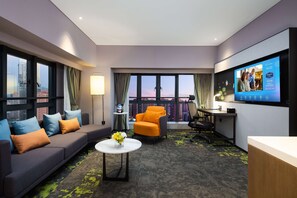 Ein modernes Hotelzimmer mit einem großen Fernseher, einem Sofa, einem orangefarbenen Sessel und einem Schreibtisch.