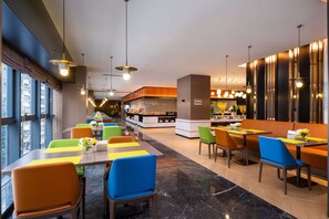 Ein modernes Restaurant mit farbenfrohen Sitzgelegenheiten, einer zentralen Küche und großen Fenstern.