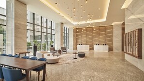 Eine moderne Hotelhalle mit Marmorboden, einer langen Holzeinbau-Rezeption und einer Sitzecke mit Sofas und Sesseln.