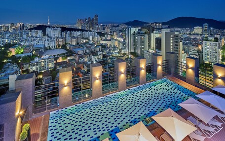 A rooftop pool with a geometric tile pattern, surrounded by modern buildings and a cityscape in the background.