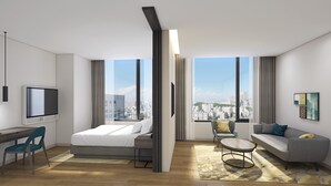 Ein modernes Hotelzimmer mit Bett, Schreibtisch und Sitzecke, mit großen Fenstern und Blick auf die Stadt.
