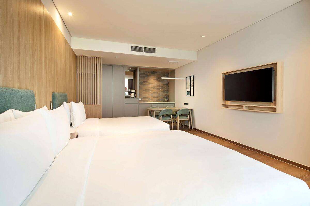 Une chambre d’hôtel avec deux lits, un coin repas et un téléviseur fixé au mur.