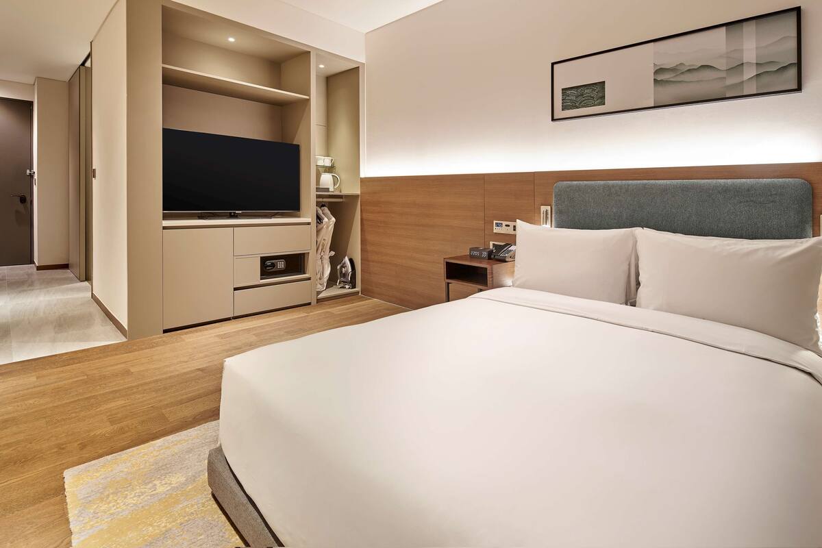 Une chambre d’hôtel avec un grand lit, une télévision, une table de chevet avec un téléphone et un tableau accroché au mur.