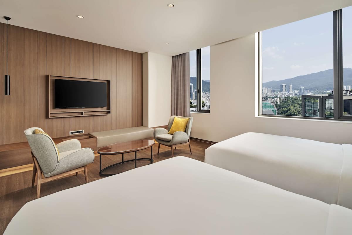 Une chambre d’hôtel moderne dotée d’un grand lit, d’un canapé, d’un fauteuil, d’une télévision et offrant une vue sur la ville.