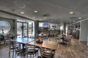 A spacious restaurant with high ceilings, wooden tables and chairs, and a bar area.
