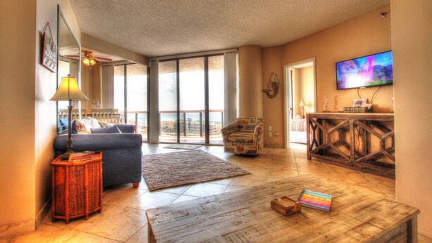 A spacious living room with a sofa, coffee table, and a television. - Beach Front Condo with ocean and pool view!!! (Miramar Beach)