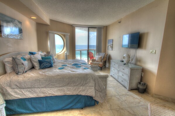 A bedroom with a large bed, a television, a chair, and a view of the ocean.