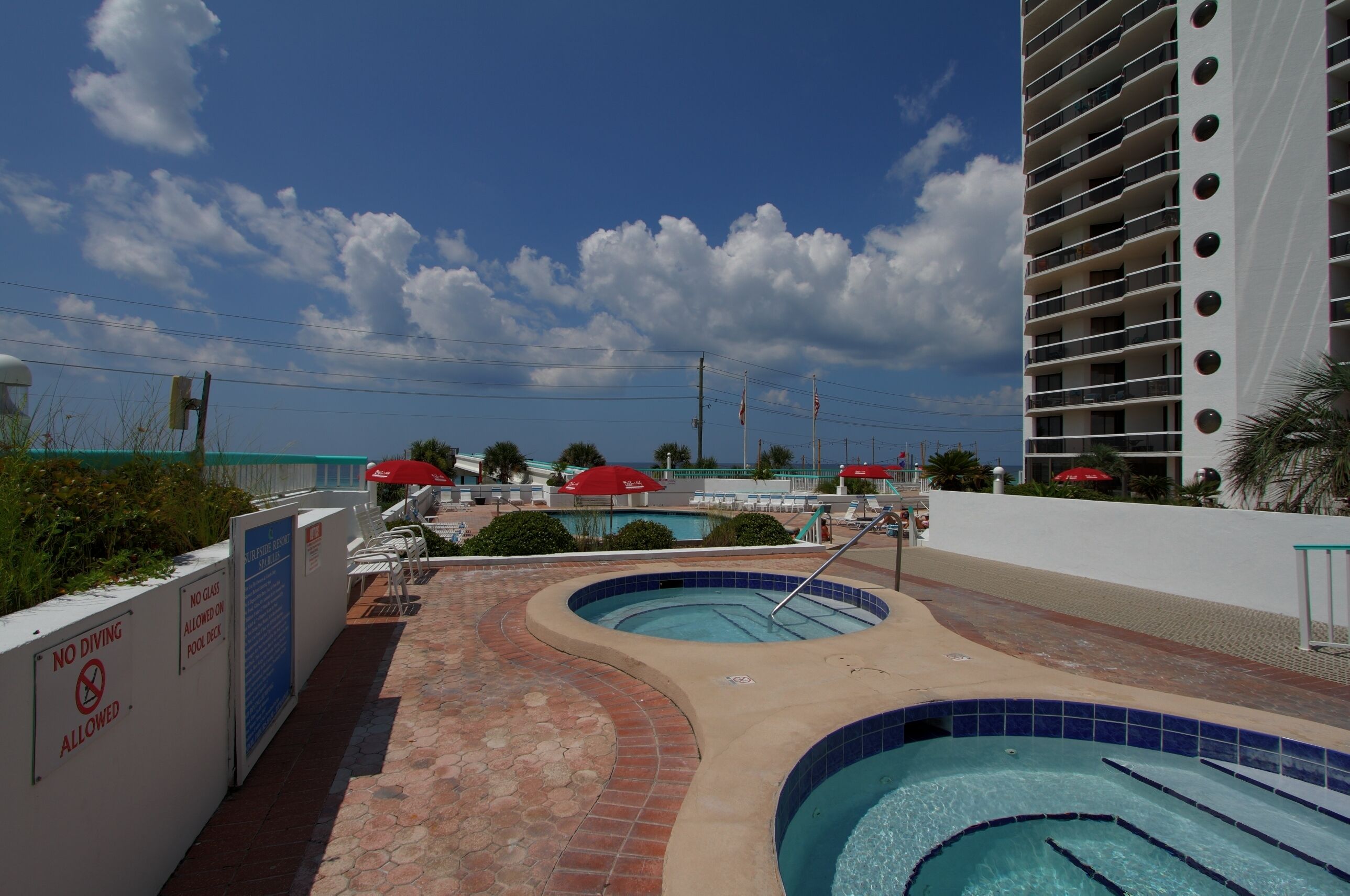 A pool area with two swimming pools, lounge chairs, and umbrellas.