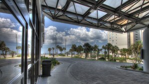 A covered outdoor area with a curved pathway, palm trees, and a view of a building in the background. - Beach Front Condo with ocean and pool view!!! (Miramar Beach)
