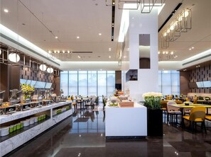 A modern hotel lobby with a central reception desk, multiple dining areas, and a large window providing a view of the cityscape. - Hampton BY Hilton Nanning Wuxiang (Nanning)