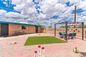 Relax in a serene outdoor space with a brick building backdrop, featuring a turf lawn, seating area, and pergola.