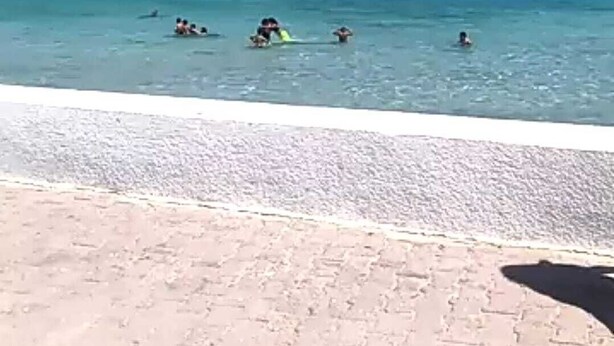 A beach with clear blue water and a few people swimming and surfing. - Tunisia, royal duplex (Salakta)