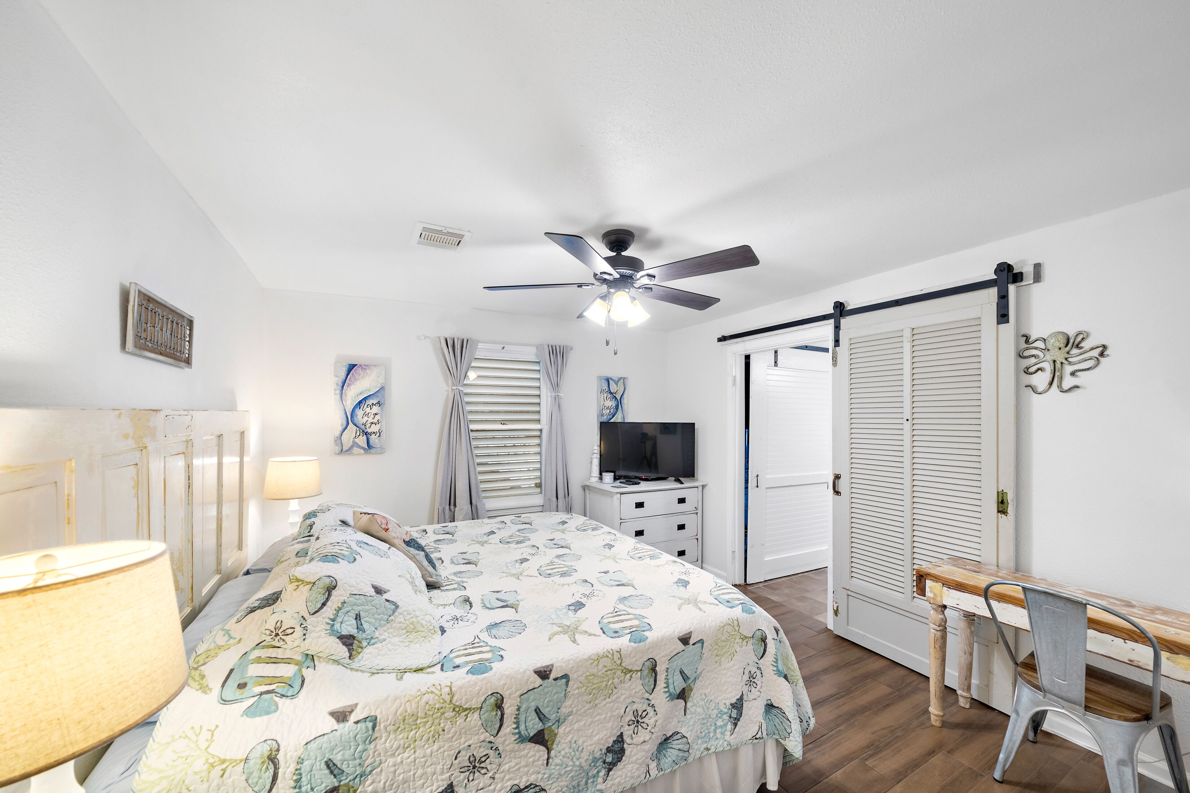 Un dormitorio con cama, escritorio, silla, ventilador de techo, televisor y armario.