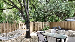 Une terrasse extérieure avec une table et des chaises en verre, entourée d’une clôture en bois et d’arbres.