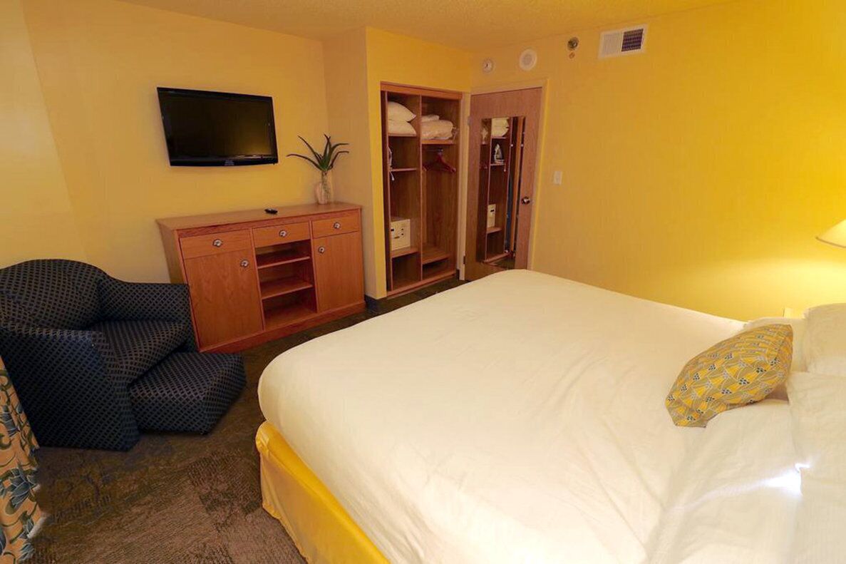 Un dormitorio con cama, televisor, armario y una silla.