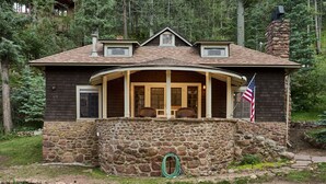 A two-story house with a stone foundation, a wrap-around porch, and a chimney. - Charming, historic, Creekside Cabin nestled at the base of Pikes Peak in Cascade (Cascade,)