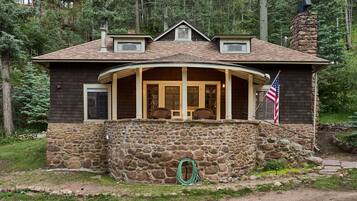 A two-story house with a stone foundation, a wrap-around porch, and a chimney.