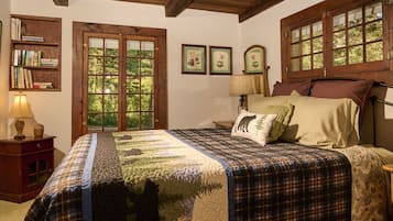 A bedroom with a large bed, a wooden headboard, a nightstand, a bookshelf, and a window with a view of trees.
