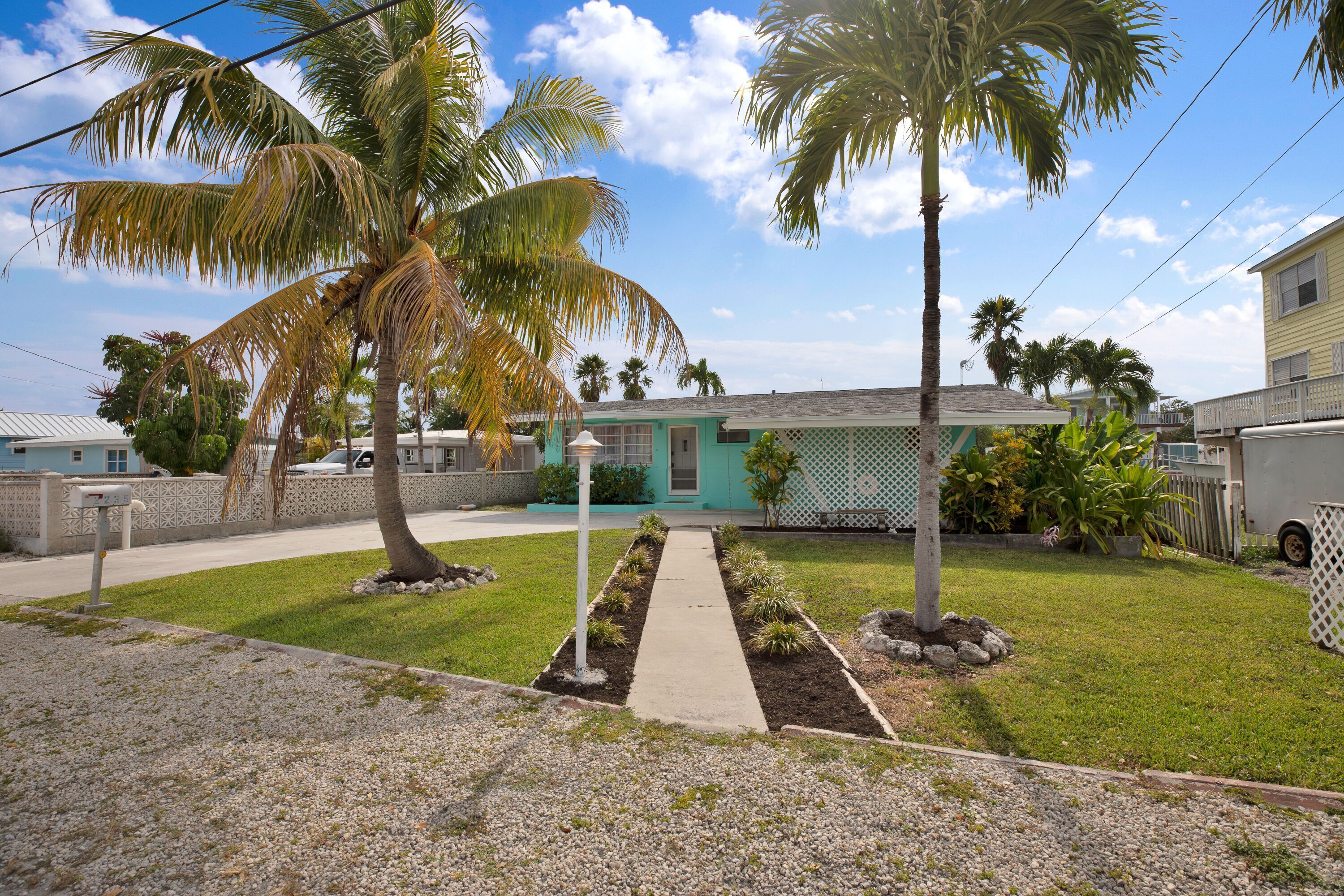 A residential property with a front yard, palm trees, a pathway, and a house with a green door.