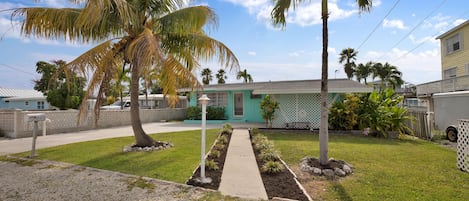 A residential property with a front yard, palm trees, a pathway, and a house with a green door.